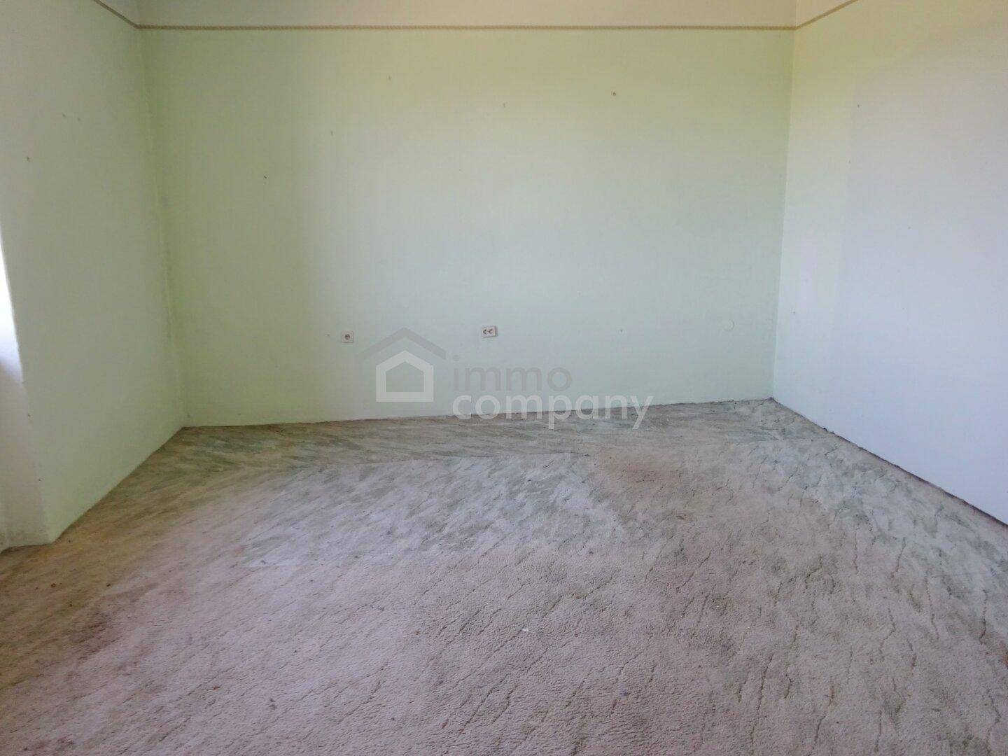 Leerer Raum mit hellgrünen Wänden und unfertigem Boden, bereit für Renovierung.