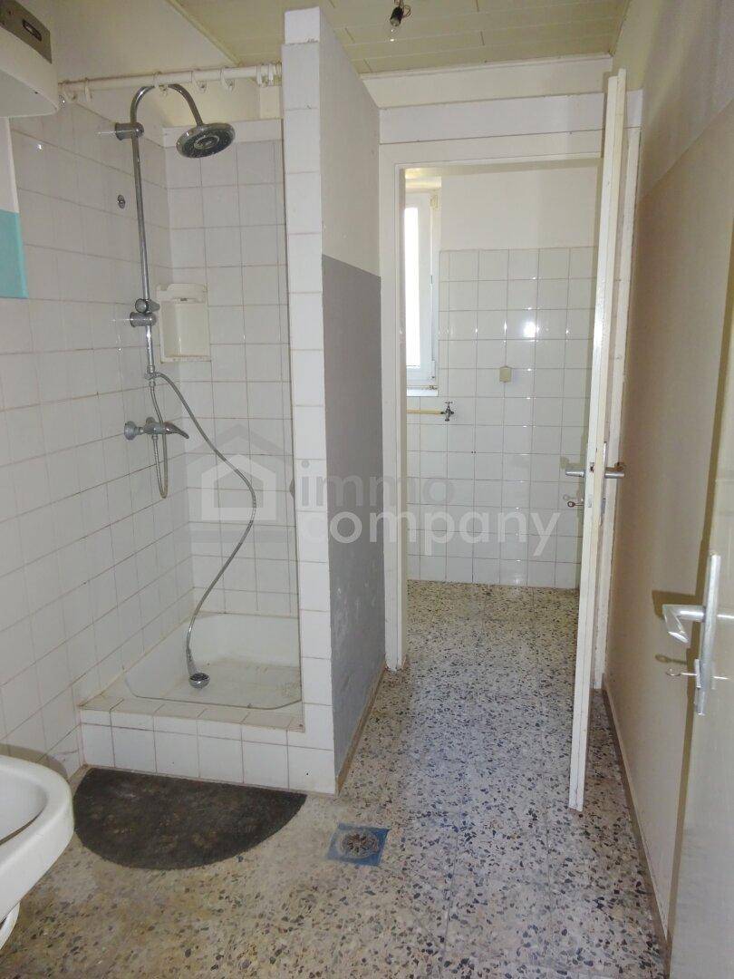 Badezimmer mit Duschbereich, Fliesenboden und einem Fenster für Tageslicht.