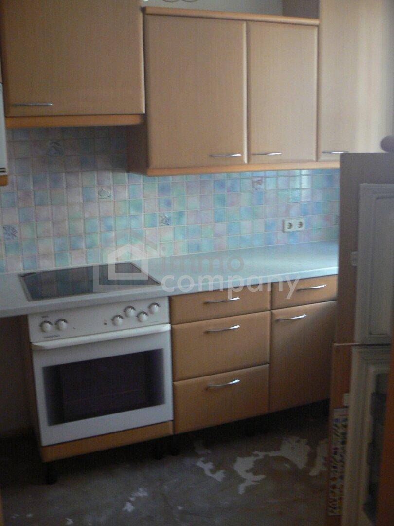 Funktionale Küche mit älteren Holzschränken, Fliesenboden und integriertem Herd mit Backofen.