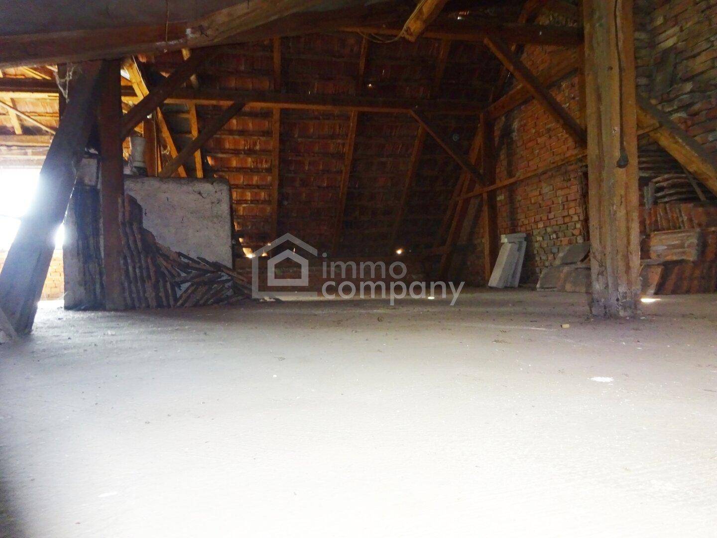 Unausgebauter Dachboden mit sichtbaren Holzbalken, Ziegelwänden und Betonboden, bereit zum Ausbau.