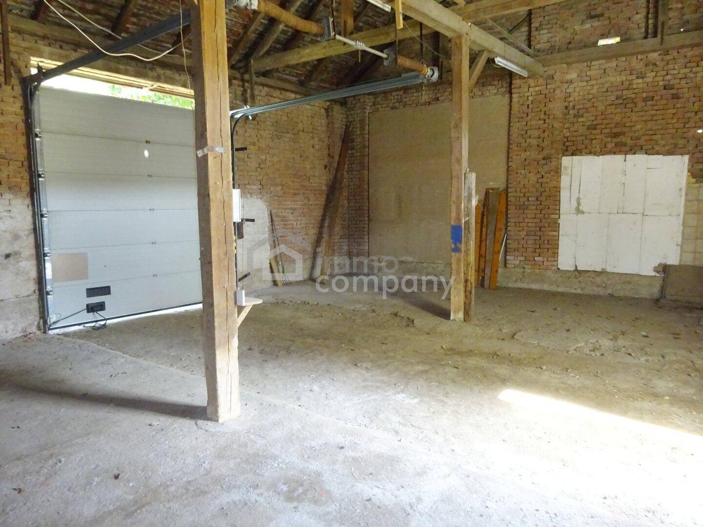 Geräumige Garage oder Scheune mit großem Tor, unverputzten Ziegelwänden und Holzbalken.