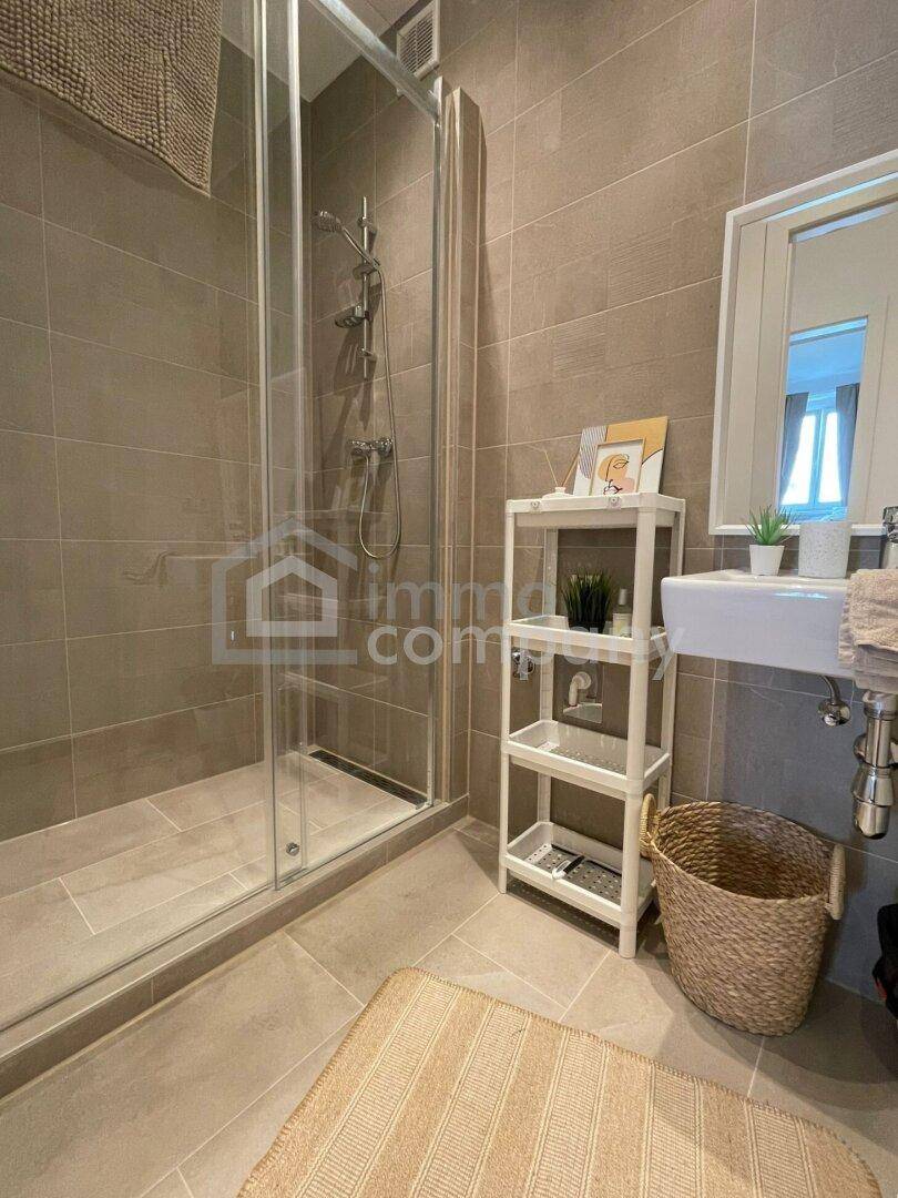 Modernes Badezimmer mit ebenerdiger Dusche, Einzelwaschbecken und grauen Fliesen.