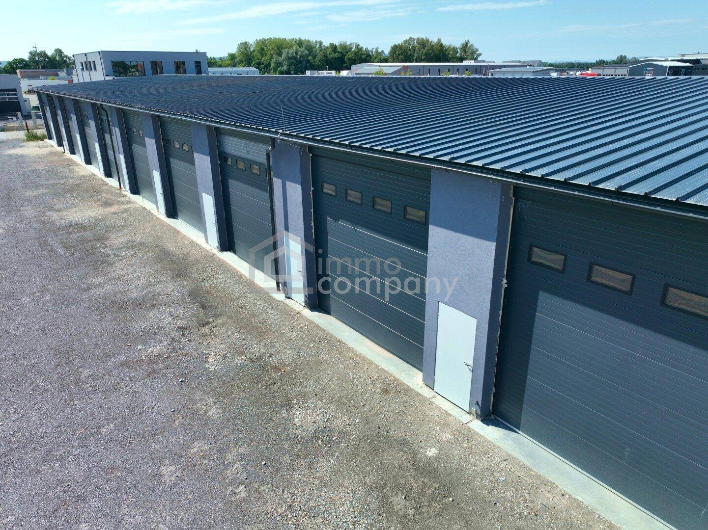 Moderne Gewerbeeinheiten mit Rolltoren und kleinen Fenstern, umgeben von einer Schotterfläche.