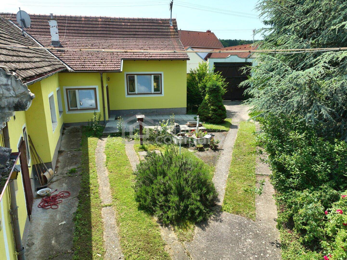 Gelbes Haus mit kleinem Vorgarten, gepflasterten Wegen und einer Garage im Hintergrund.