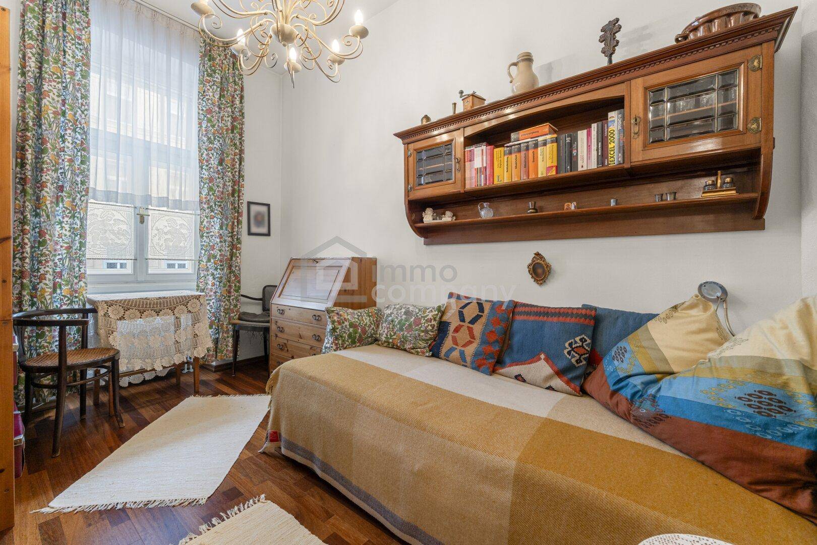 Gemütliches Zimmer mit Tagesbett, Holzregal und floralen Vorhängen, ideal als Gästezimmer.