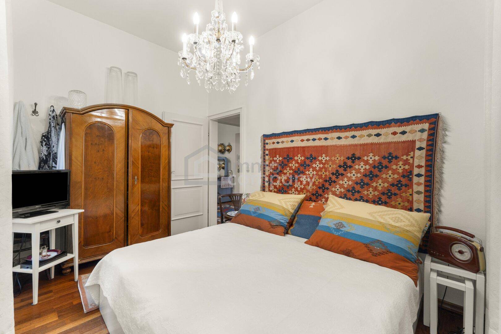 Schlafzimmer mit Doppelbett, klassischem Holzschrank und einem funkelnden Kronleuchter.