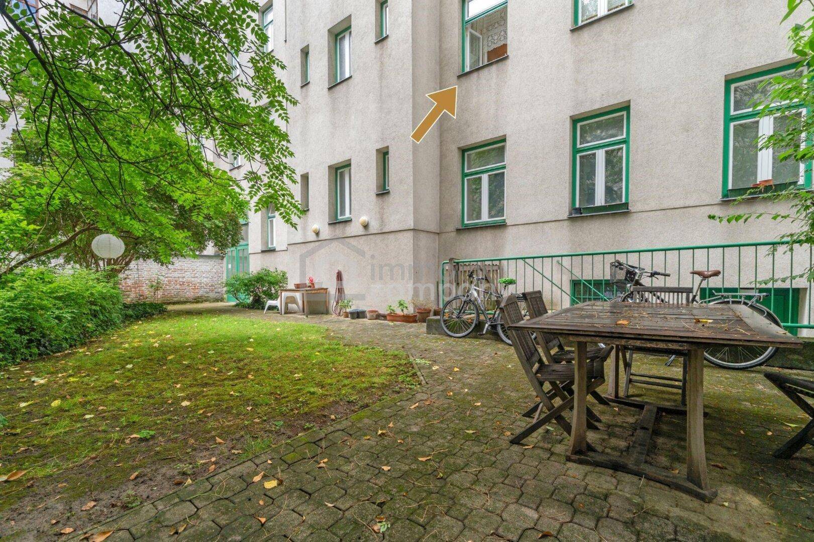 Grüner Hinterhofgarten mit Rasenfläche, Sitzgelegenheiten und Fahrradstellplätzen am Gebäude.