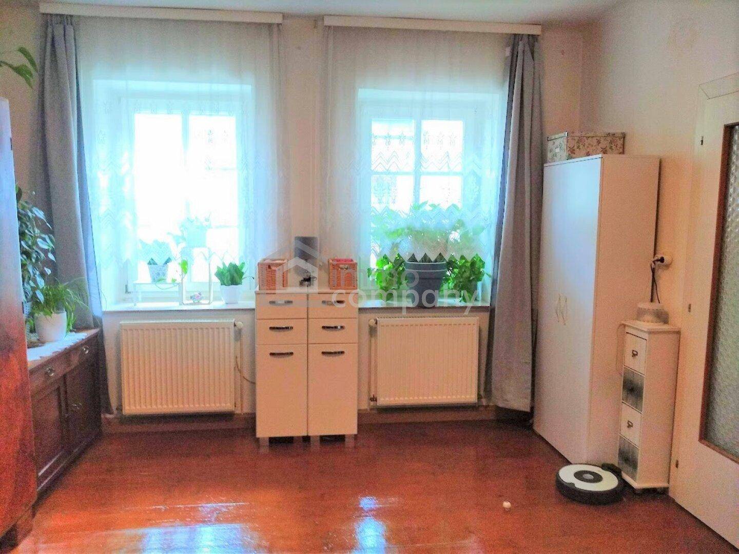 Heller Raum mit zwei Fenstern, Heizkörpern und einem Schrank, der viel Tageslicht hereinlässt.