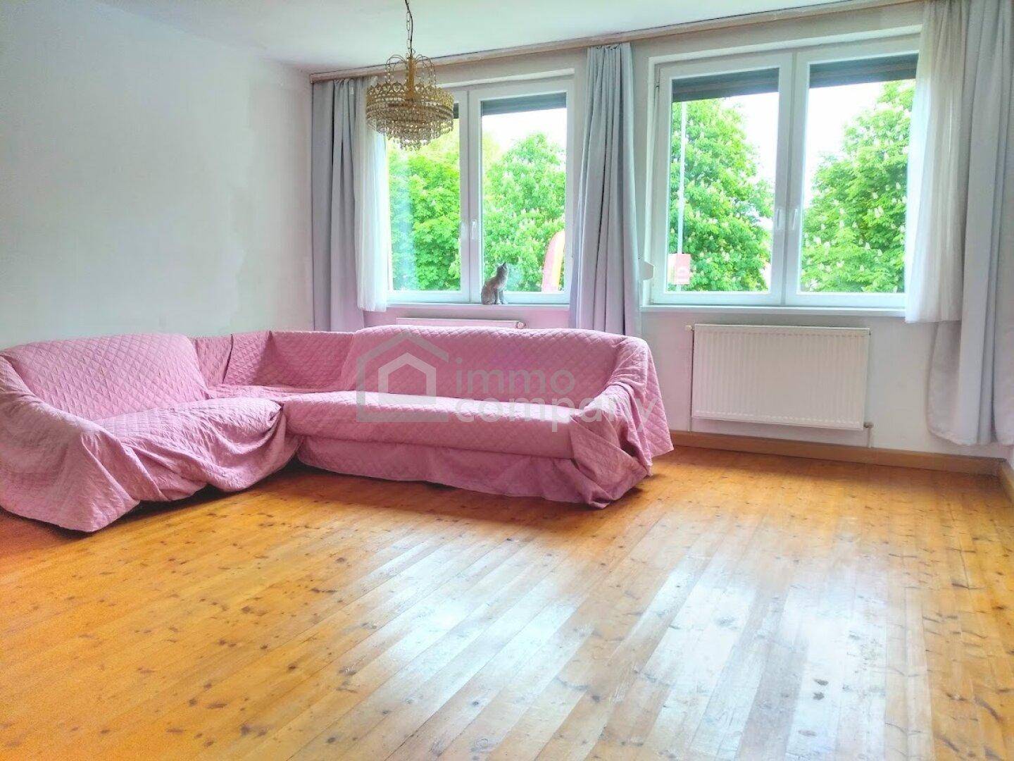 Helles Wohnzimmer mit Holzboden, großer rosa Couch und Blick ins Grüne durch die Fenster.