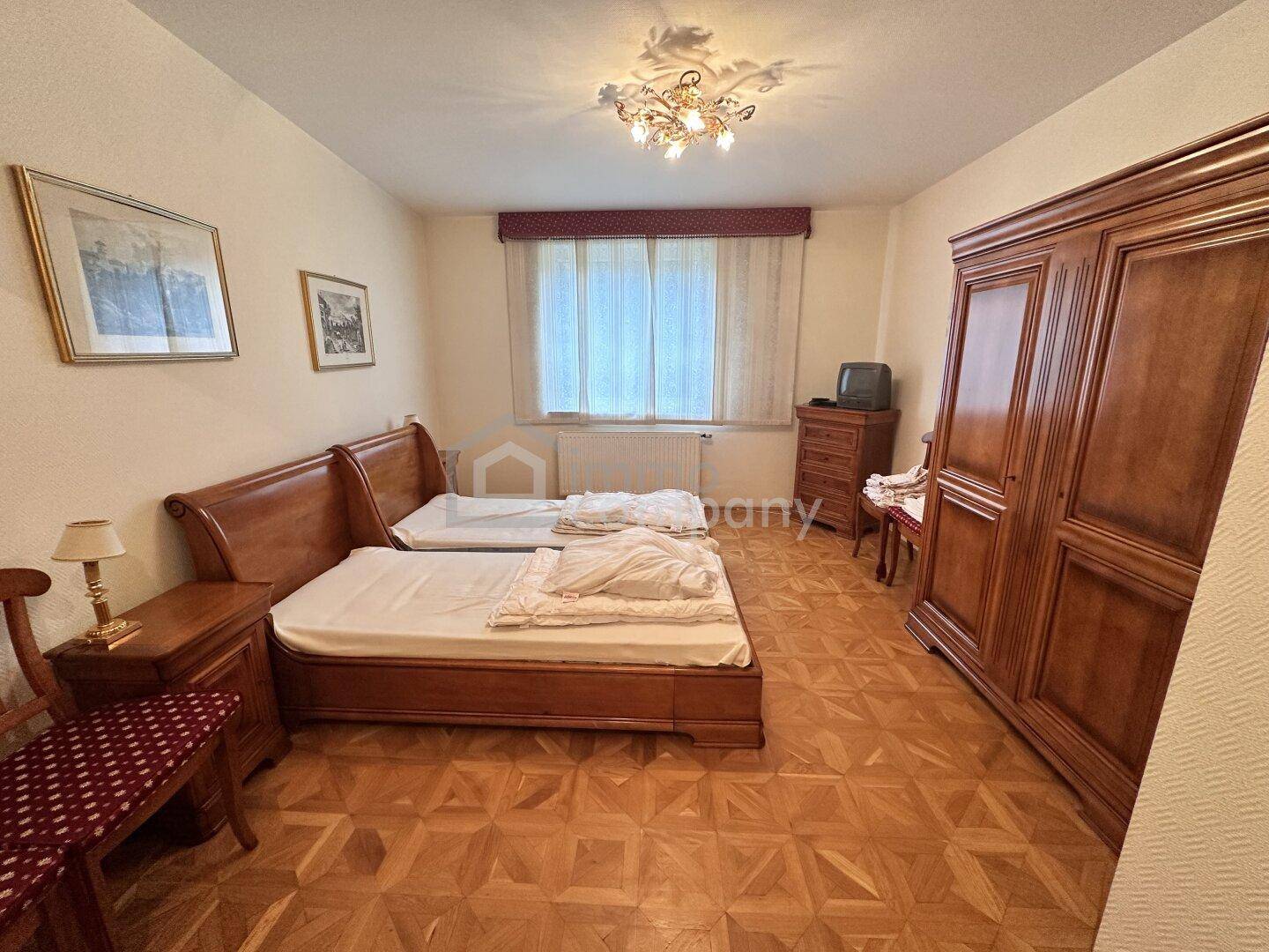 Gemütliches Schlafzimmer mit zwei Einzelbetten, Holzschrank und Fenster mit Vorhängen.