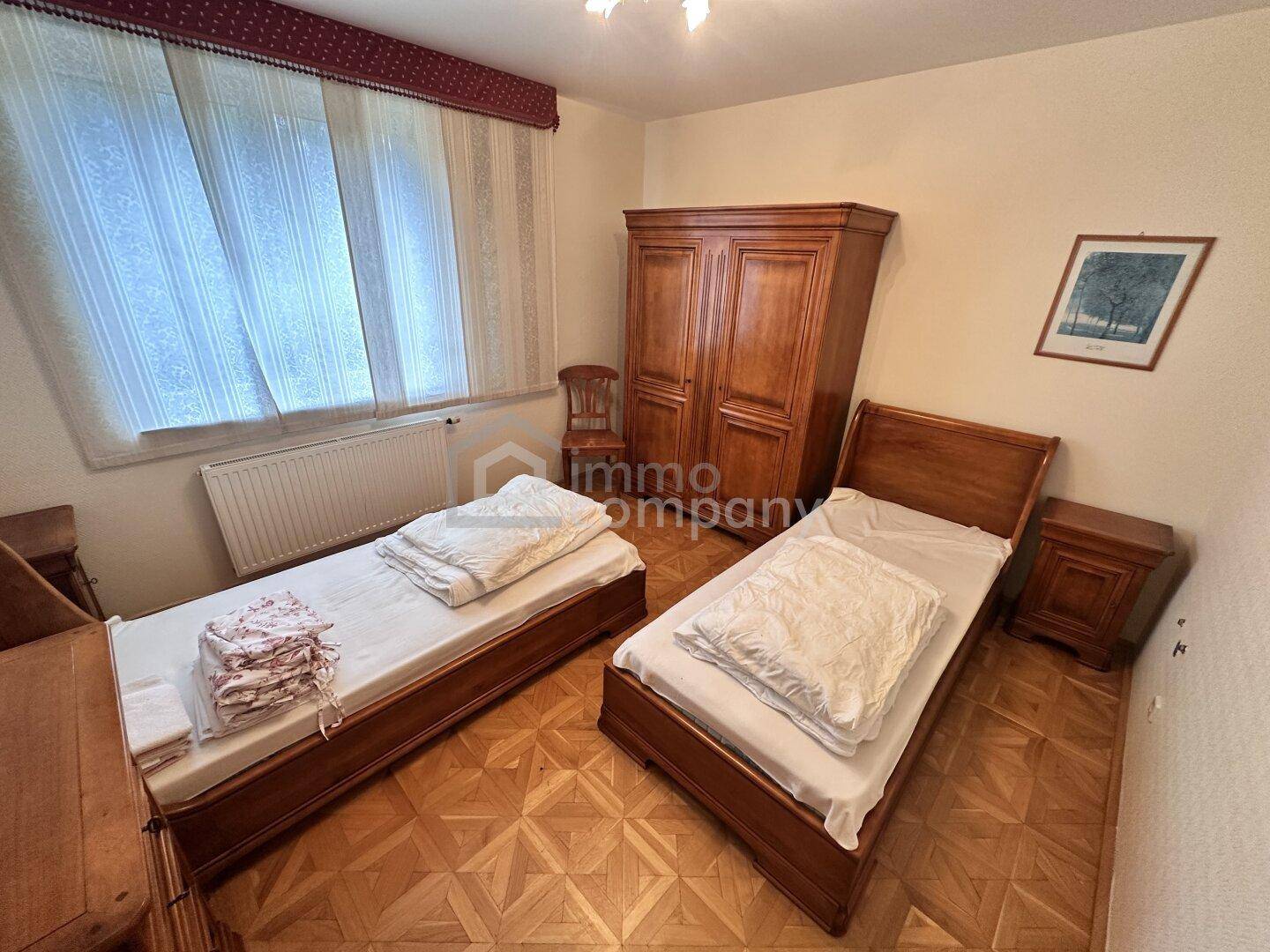 Helles Schlafzimmer mit zwei Einzelbetten, Holzmöbeln und Blick zum Fenster.