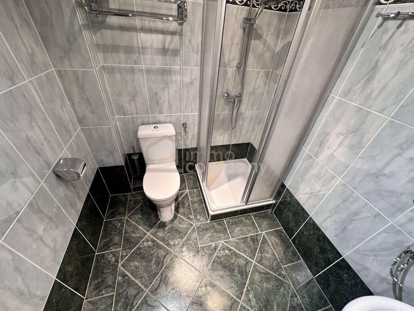 Modern gefliestes Badezimmer mit Duschkabine und Toilette in Grautönen.