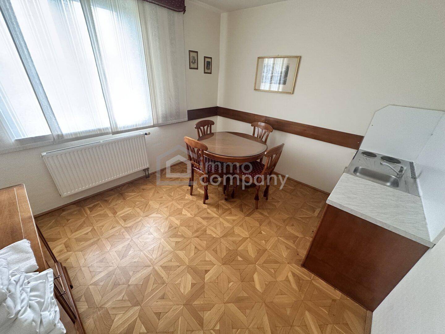 Kleiner Essbereich mit rundem Holztisch, Stühlen und einer integrierten Kochnische mit Kochfeld und Spüle.