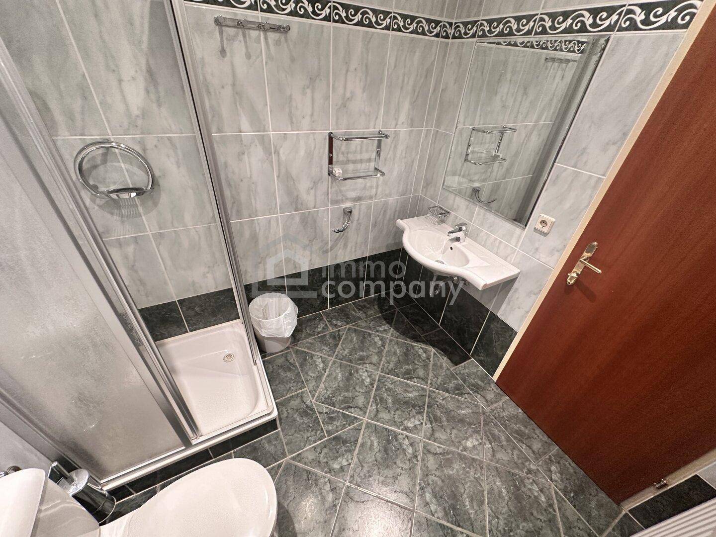 Gefliestes Badezimmer mit Duschkabine, Waschbecken, Toilette und einem großen Wandspiegel.