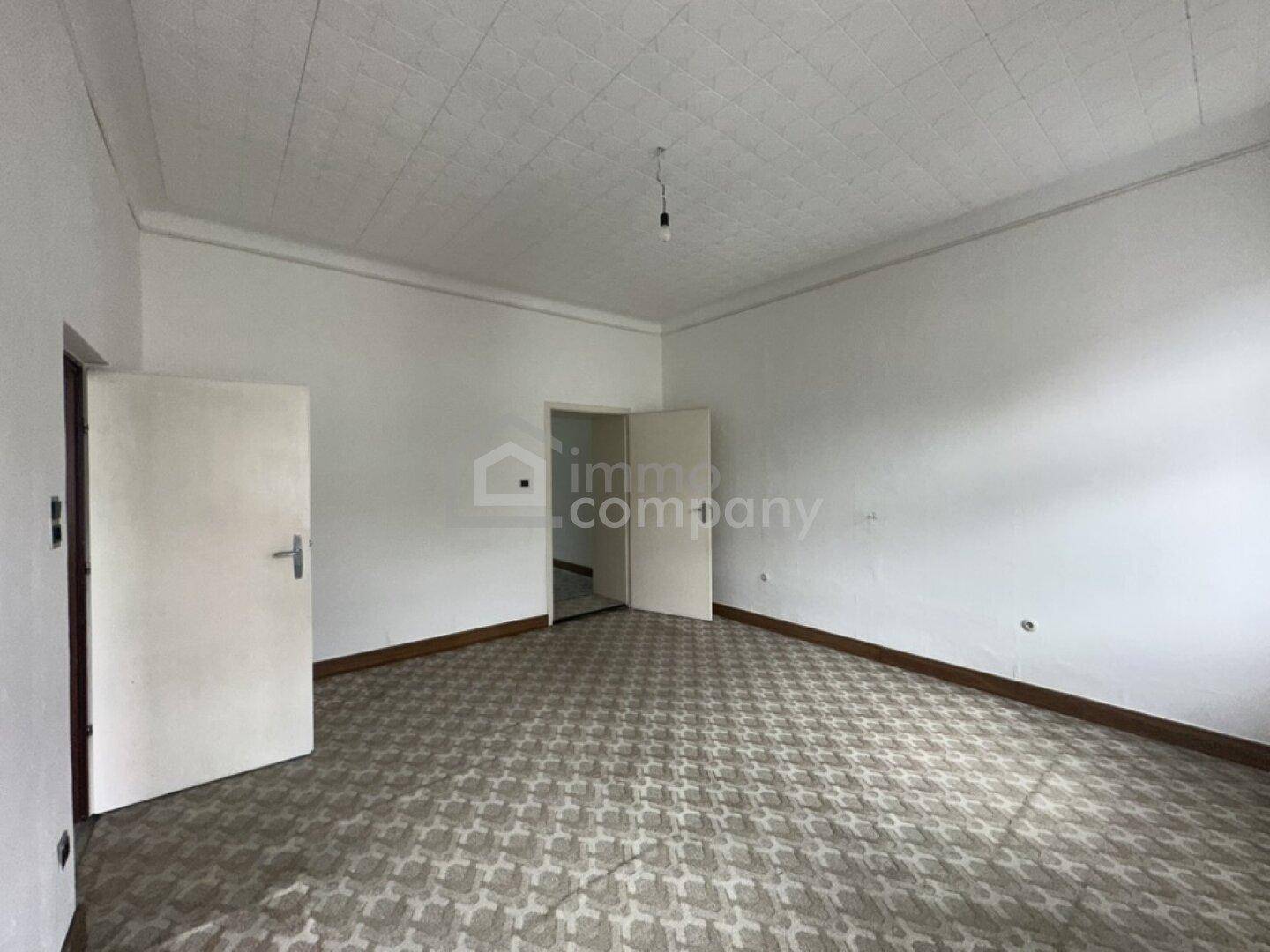 Geräumiges Zimmer mit gemustertem Bodenbelag und zwei Türen, ideal für eine Renovierung.