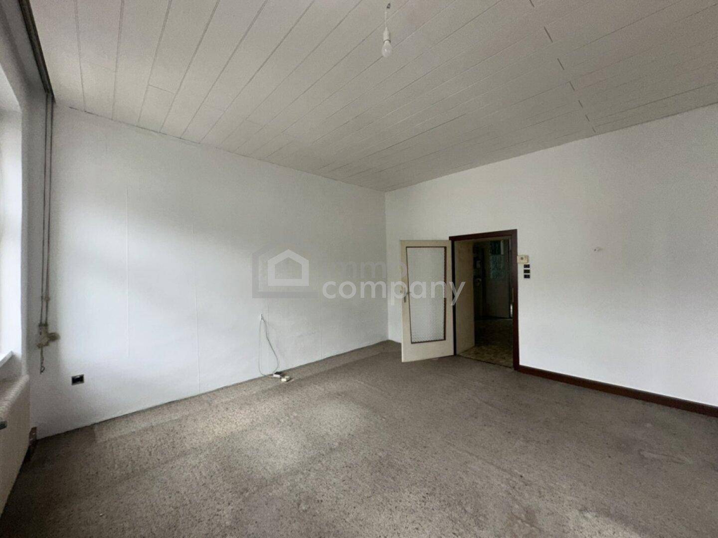 Unmöblierter Raum mit Fenster, Tür und Holzpaneeldecke, bereit zur Renovierung.