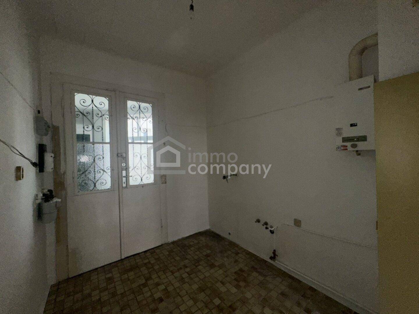 Küchenbereich mit alten Fliesen, Wasseranschlüssen und einer Tür mit dekorativem Glas.