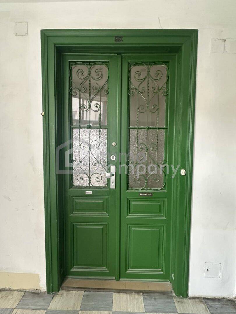 Grüne Eingangstür mit dekorativen Eisengittern und Glasdetails eines Altbaus.