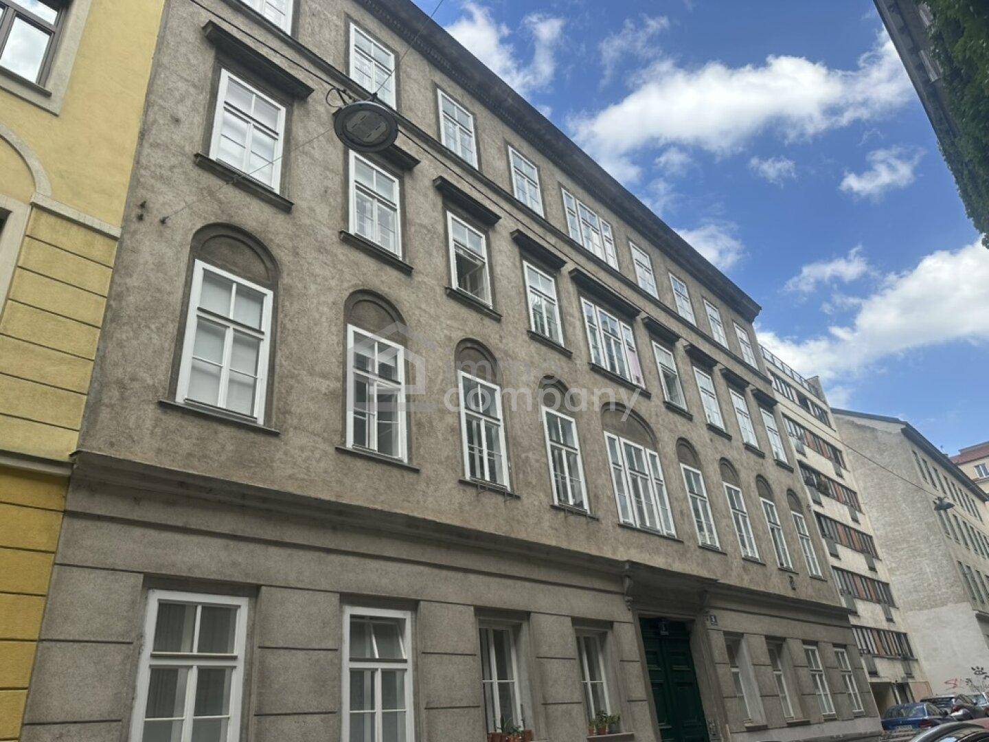 Historisches Gebäude mit grauer Fassade und vielen Fenstern an einer städtischen Straße.