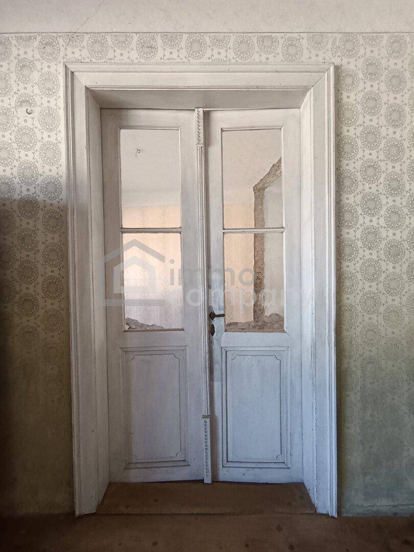 Alte weiße Doppeltür mit Glaseinsätzen und gemusterter Tapete in einem Innenraum.