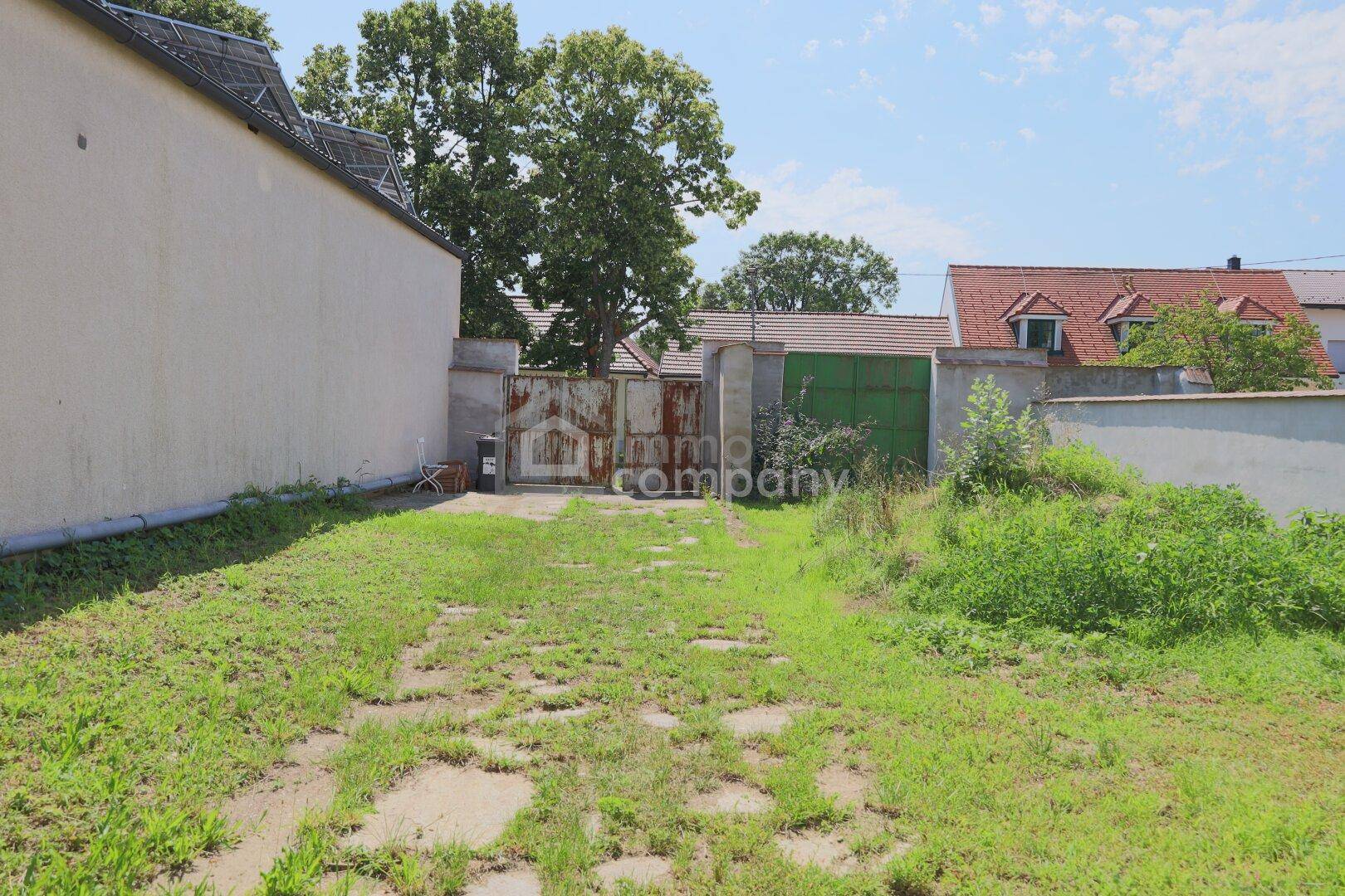Ungepflegter Gartenbereich mit Zufahrt und alten Toren, umgeben von Gebäuden.