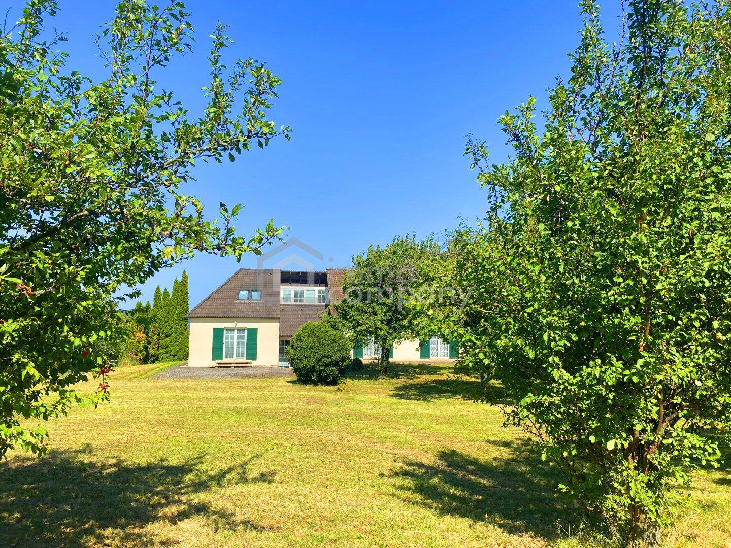 Weitläufiger Garten mit altem Baumbestand und Blick auf das charmante Landhaus an einem sonnigen Tag.