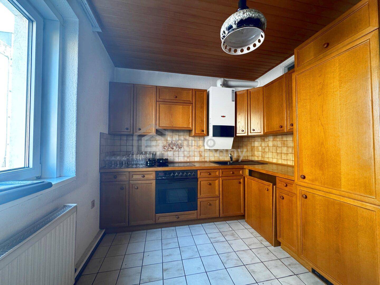Funktionale Küche mit Holzschränken, Fliesenboden und einem Gasboiler an der Wand.