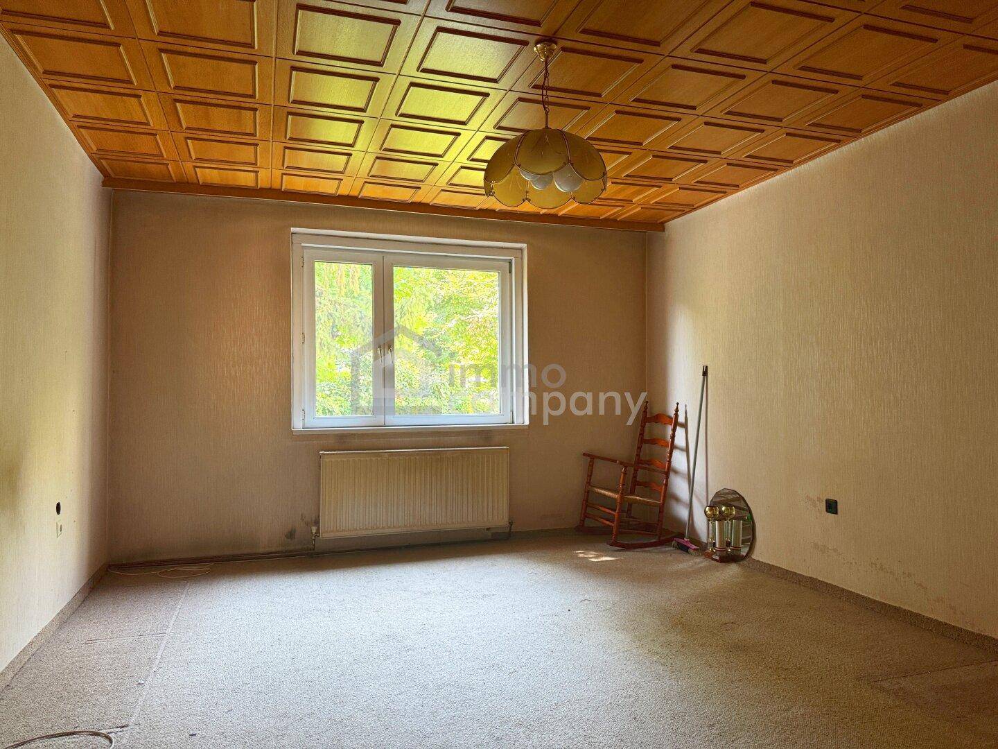 Geräumiges Zimmer mit Holzpaneeldecke, Teppichboden und einem Fenster mit Blick ins Grüne.