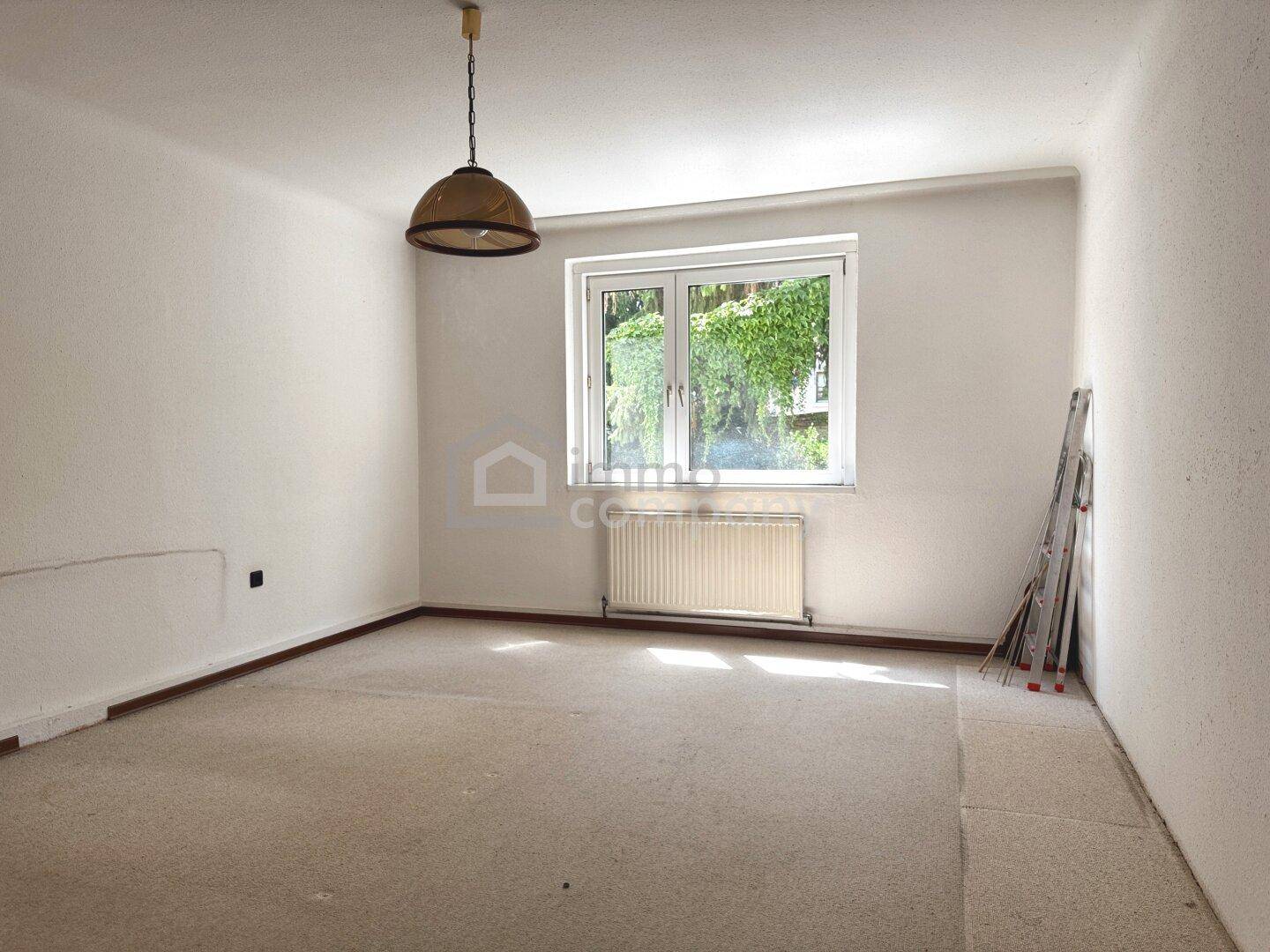 Helles, unmöbliertes Zimmer mit weiß gestrichenen Wänden, einem Fenster und Heizkörper.