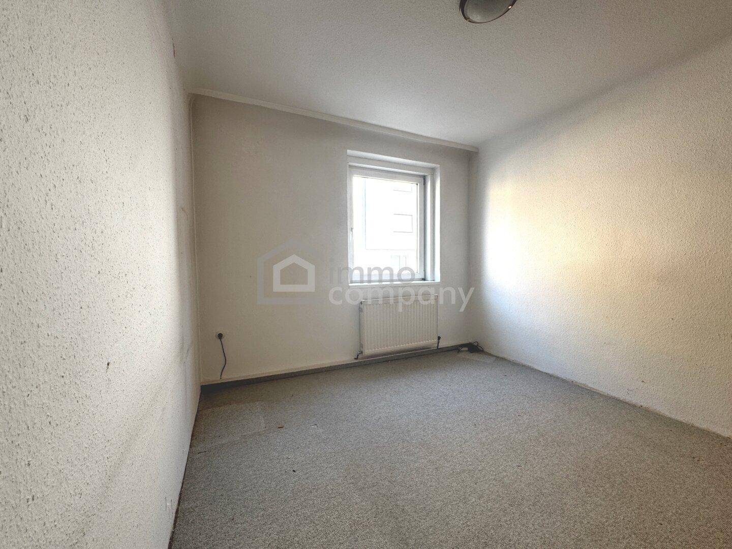 Kleines, helles Schlafzimmer mit Teppichboden, weiß gestrichenen Wänden und einem Fenster.