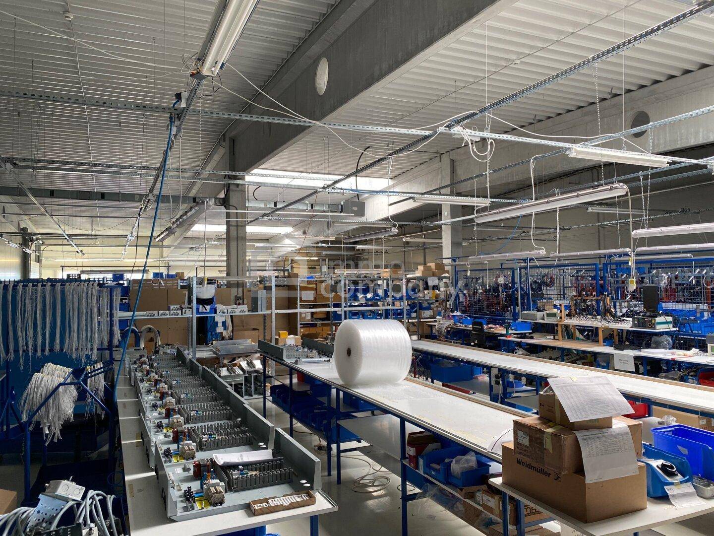 Produktionshalle mit Montagelinien, Arbeitsplätzen und industrieller Beleuchtung.