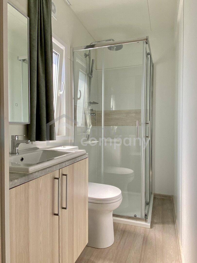 Modernes Badezimmer mit Duschkabine, Waschbecken und WC, hell durch ein Fenster.