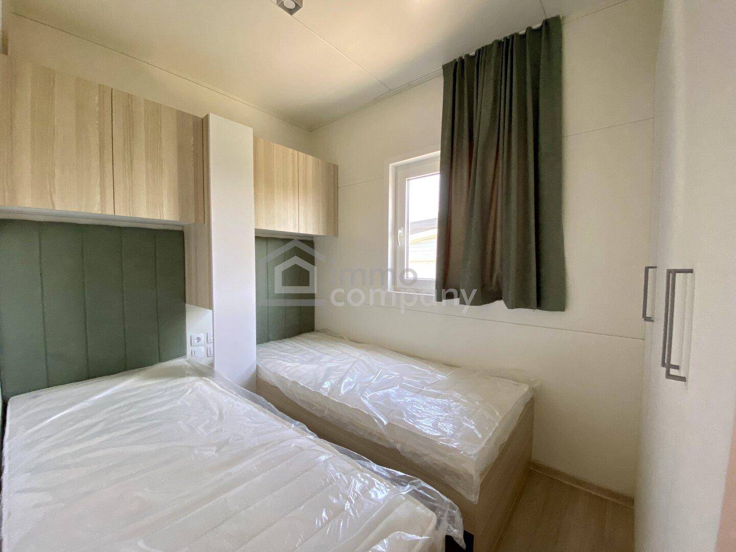 Schlafzimmer mit zwei Einzelbetten und praktischen Oberschränken, hell durch ein Fenster.