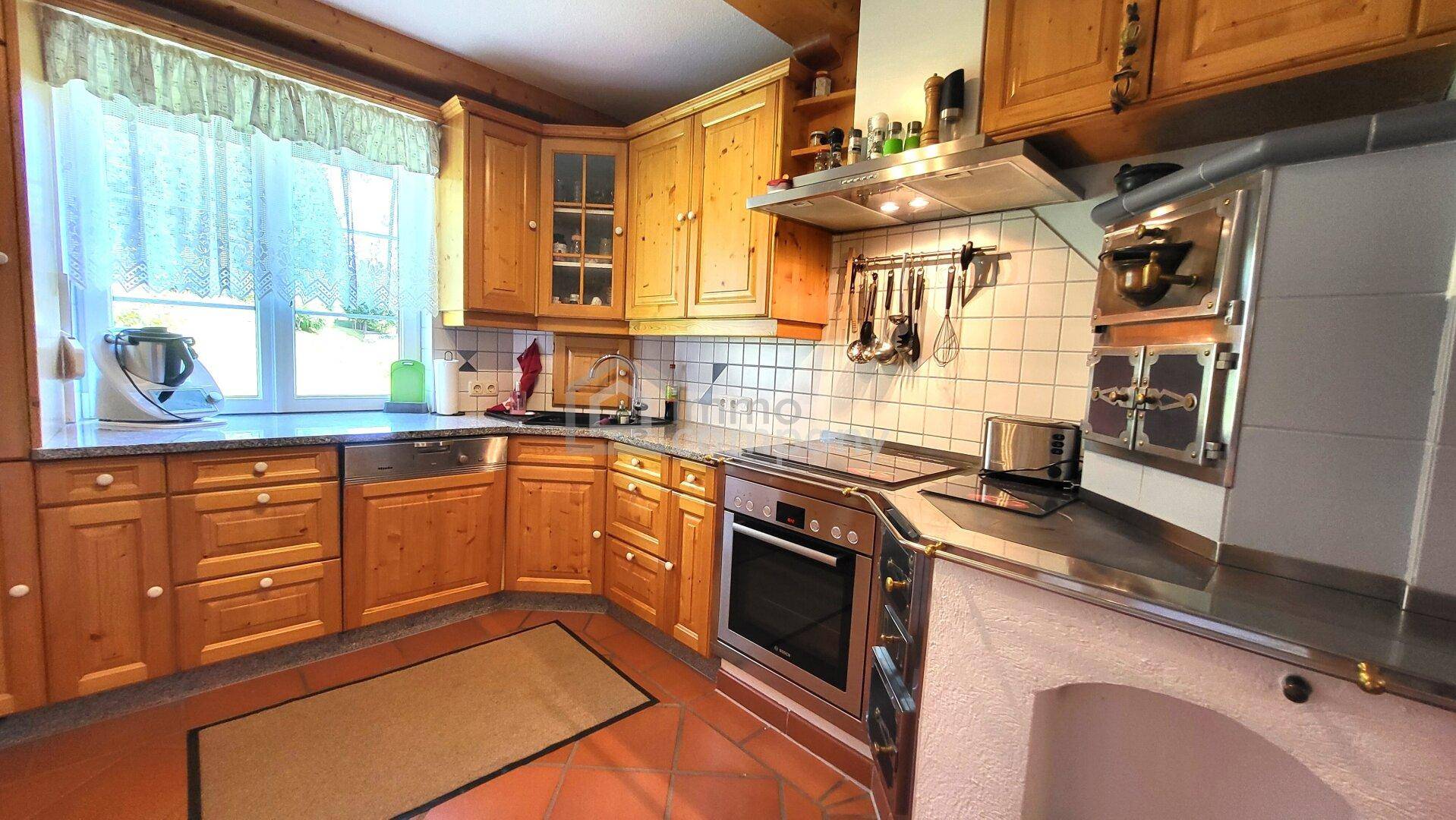 Traditionelle Holzküche mit Einbaugeräten, Fliesenboden und Fenster mit Vorhang.