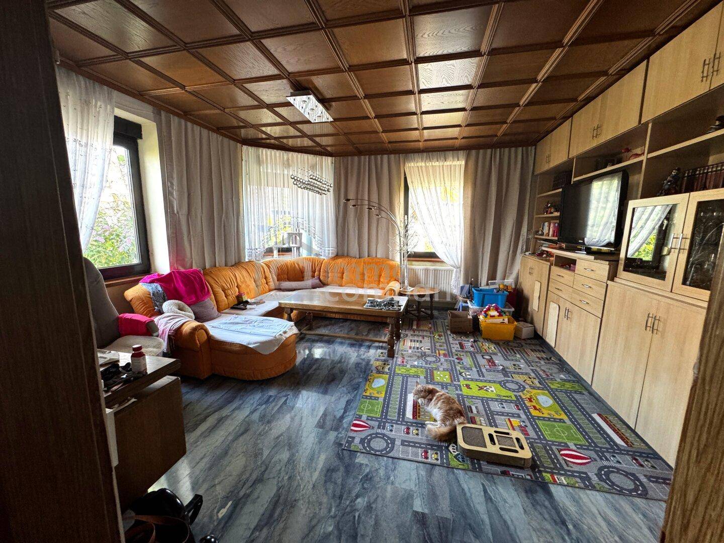 Geräumiges Wohnzimmer mit bequemer Couch, Holzdecke, Fliesenboden und bunten Dekorationen.