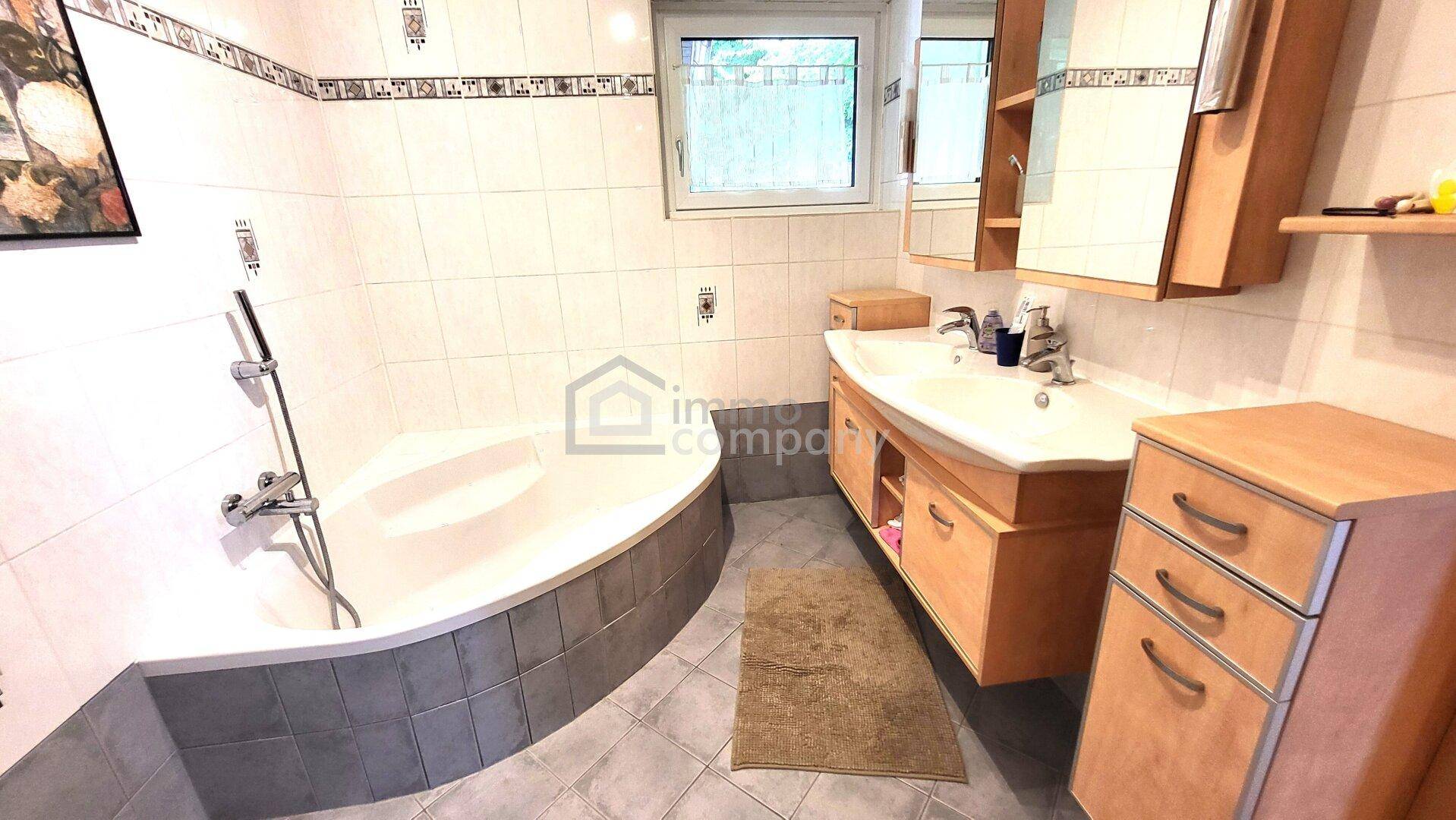 Helles Badezimmer mit Eckbadewanne, Doppelwaschbecken und Fenster für Tageslicht.
