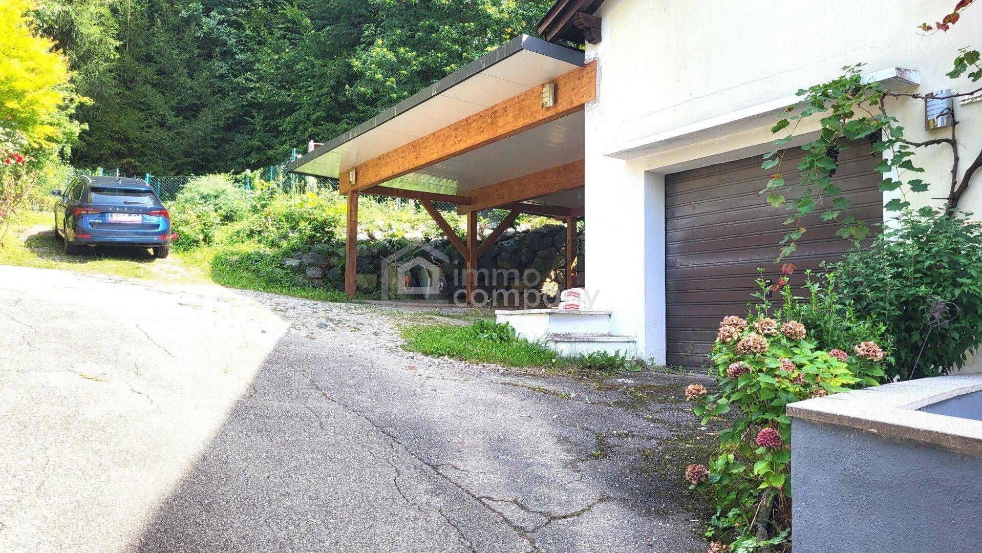 Einfahrt zum Haus mit Carport und Garagentor, umgeben von Bäumen und Natur.