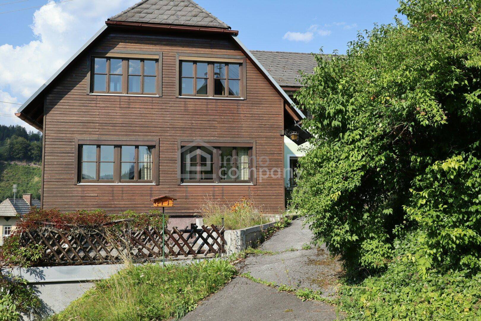 Traditionelles Holzhaus mit Satteldach und grüner Umgebung an einem sonnigen Tag.