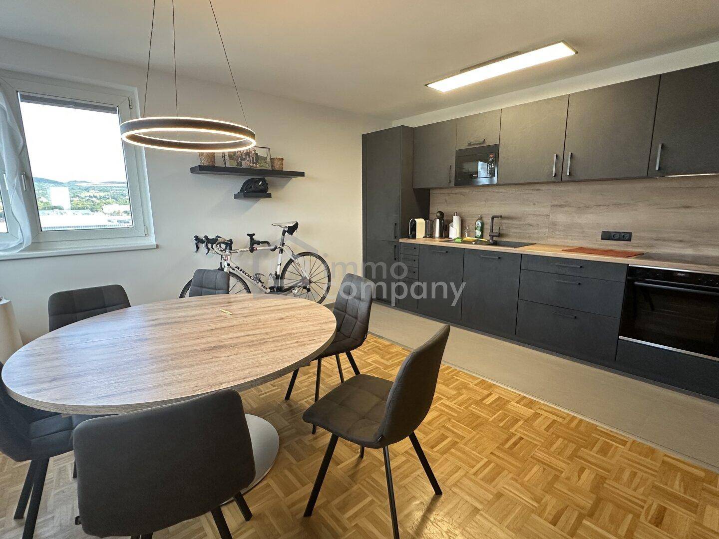 Moderne Küche mit dunklen Schränken, Holzarbeitsplatte und Essbereich mit Stadtblick.
