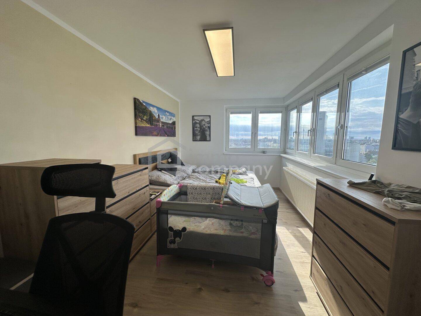 Helles Schlafzimmer mit Babybett, Holzkommoden und weitem Blick auf die Stadt.