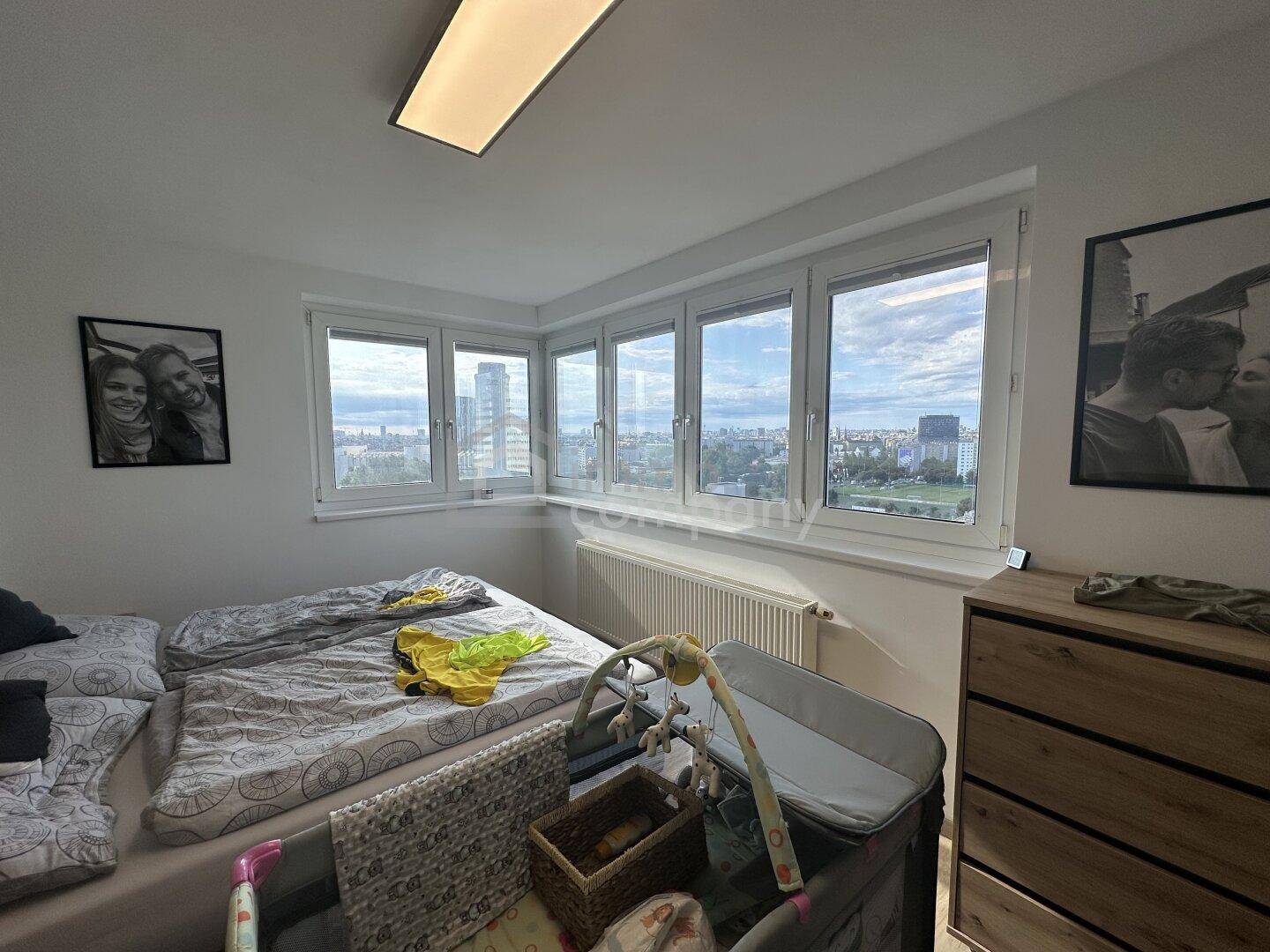 Gemütliches Schlafzimmer mit Doppelbett, Babybett und hellem Ausblick auf die Stadtlandschaft.