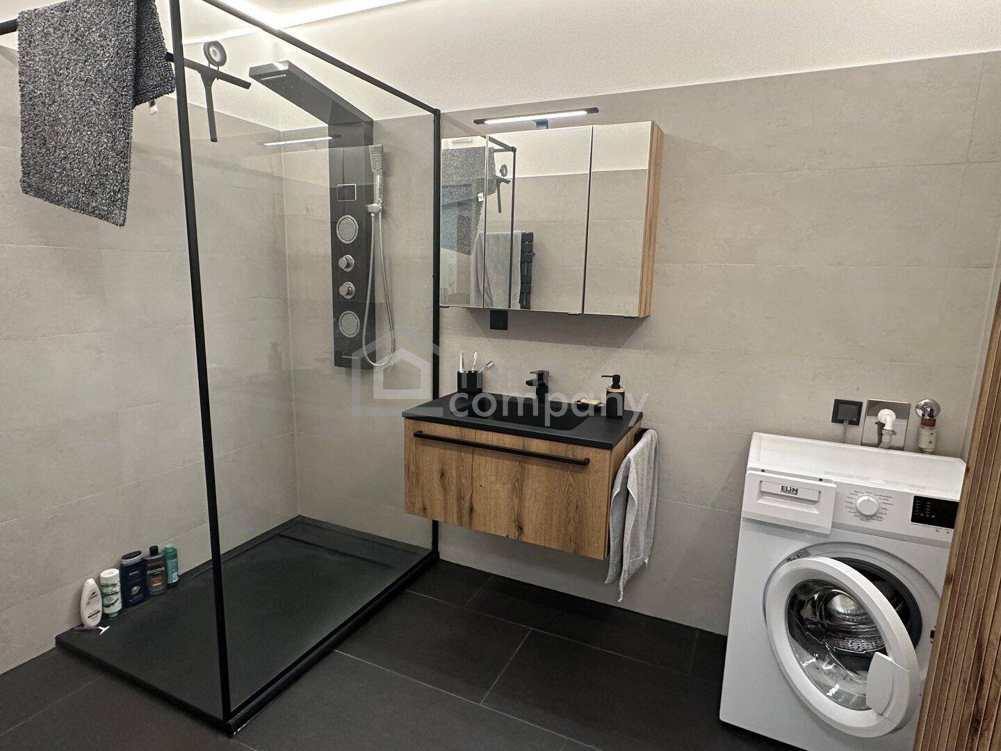 Modernes Badezimmer mit ebenerdiger Dusche, schwebendem Waschtisch und Waschmaschine.