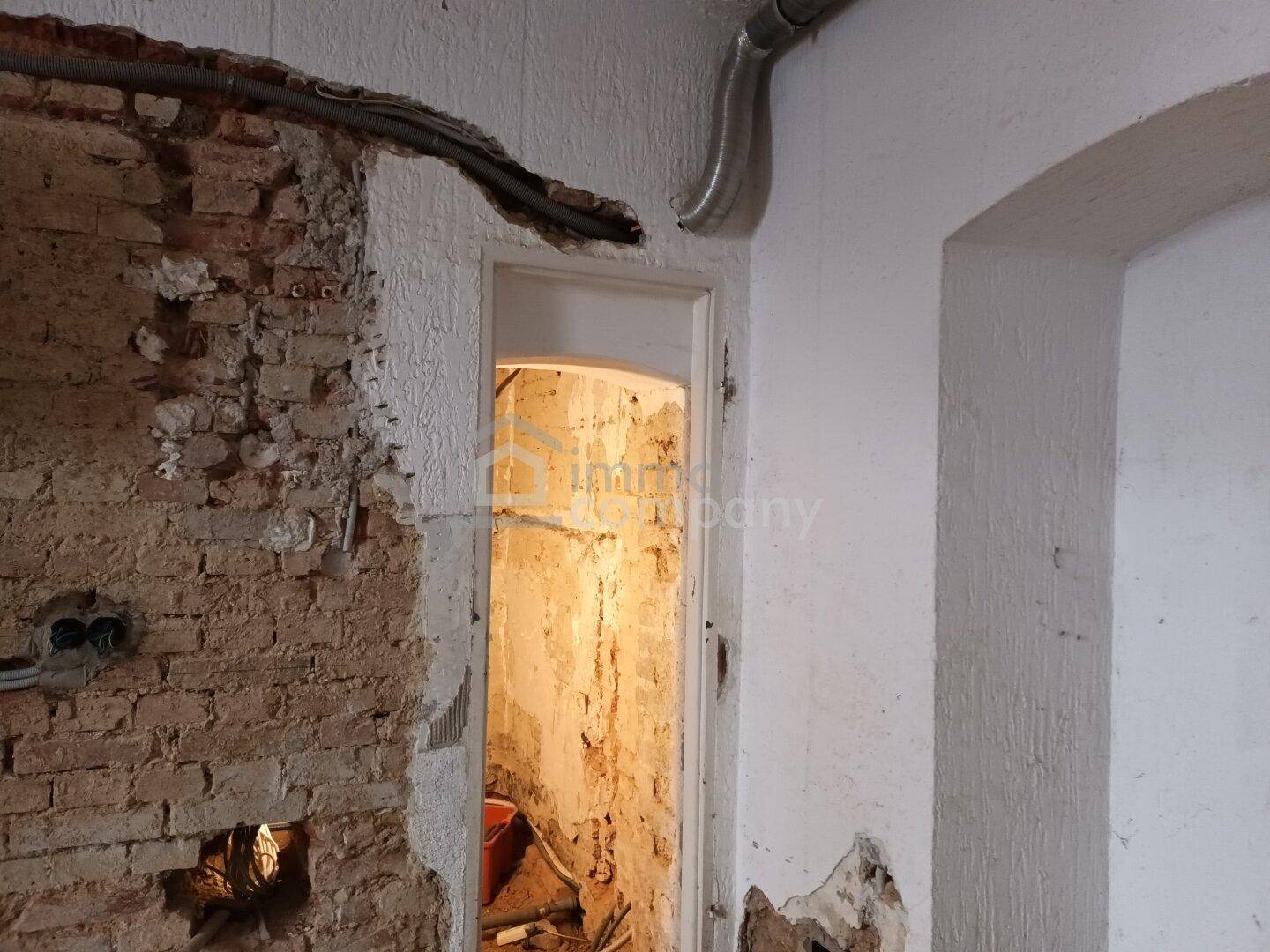 Detailansicht eines Türrahmens in einem Raum im Rohbau mit freigelegten Ziegeln und Leitungen.