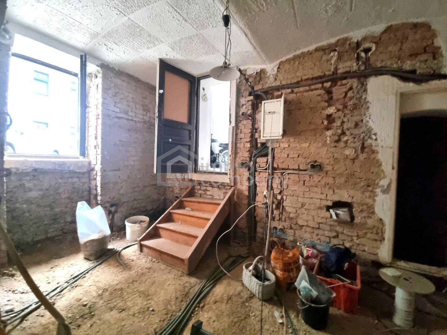 Rohbau-Innenraum mit freigelegten Ziegelwänden, einer Holztreppe und Fenstern für Tageslicht.