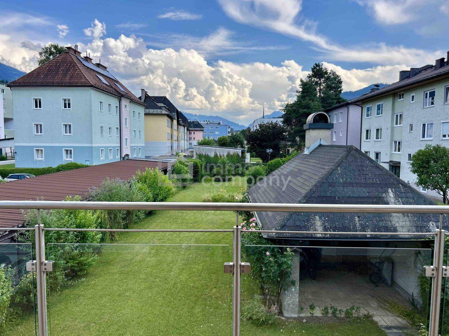 Blick vom Balkon über den Garten auf die umliegenden Gebäude und die Bergkulisse.