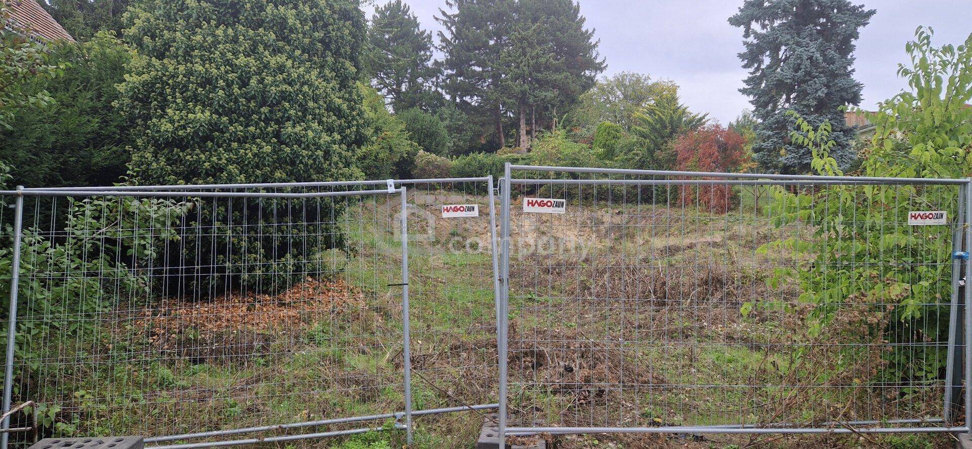Eingezäuntes Grundstück mit unebenem Gelände und dichter Vegetation, bereit zur Bebauung.