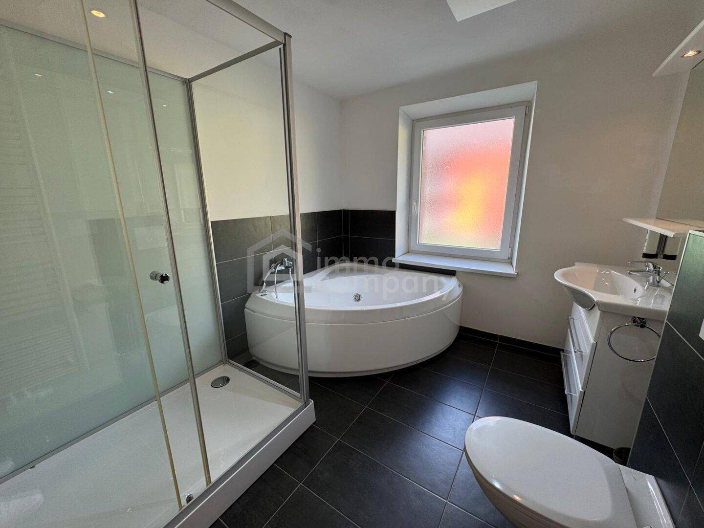 Modernes Badezimmer mit Eckbadewanne, Duschkabine, Waschbecken und Fenster.