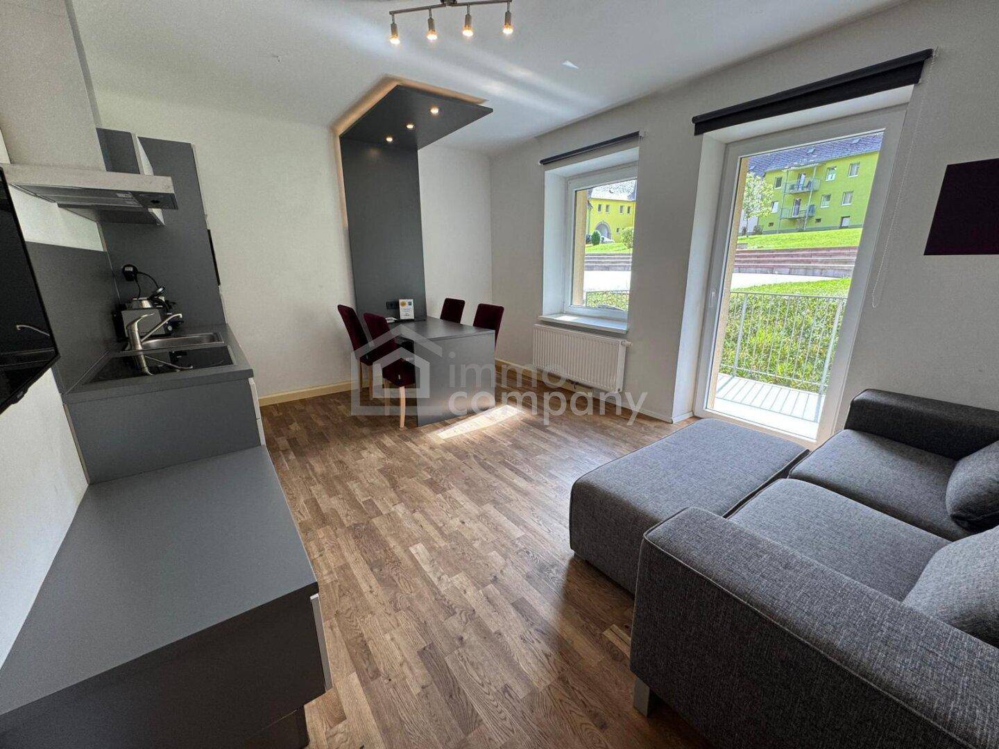 Offener Wohnbereich mit kleiner Küchenzeile, Essplatz und Zugang zu einem Balkon.