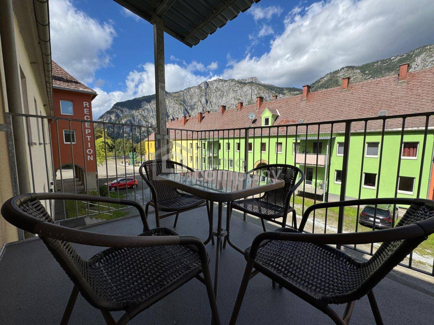 Balkon mit Sitzgelegenheiten und weitem Blick auf die Berge und umliegenden Gebäude.