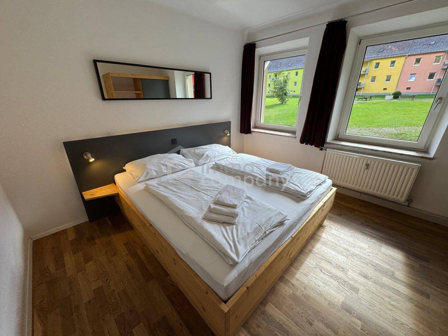 Helles Schlafzimmer mit Doppelbett, Holzboden und Blick ins Grüne.
